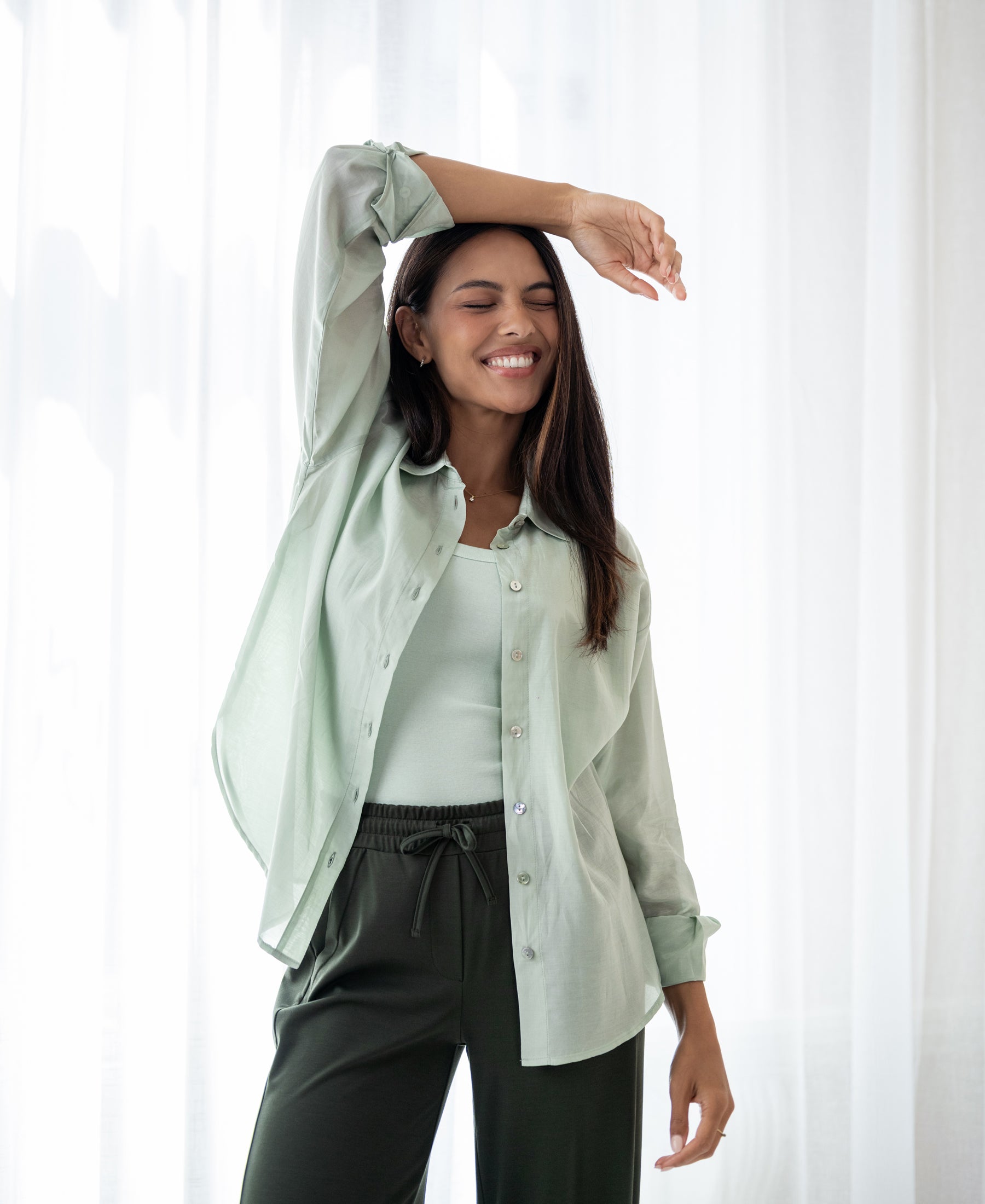 Light green LA SOYEUSE sheer oversized blouse by PLEIN PUBLIQUE, shown in front of white curtains.