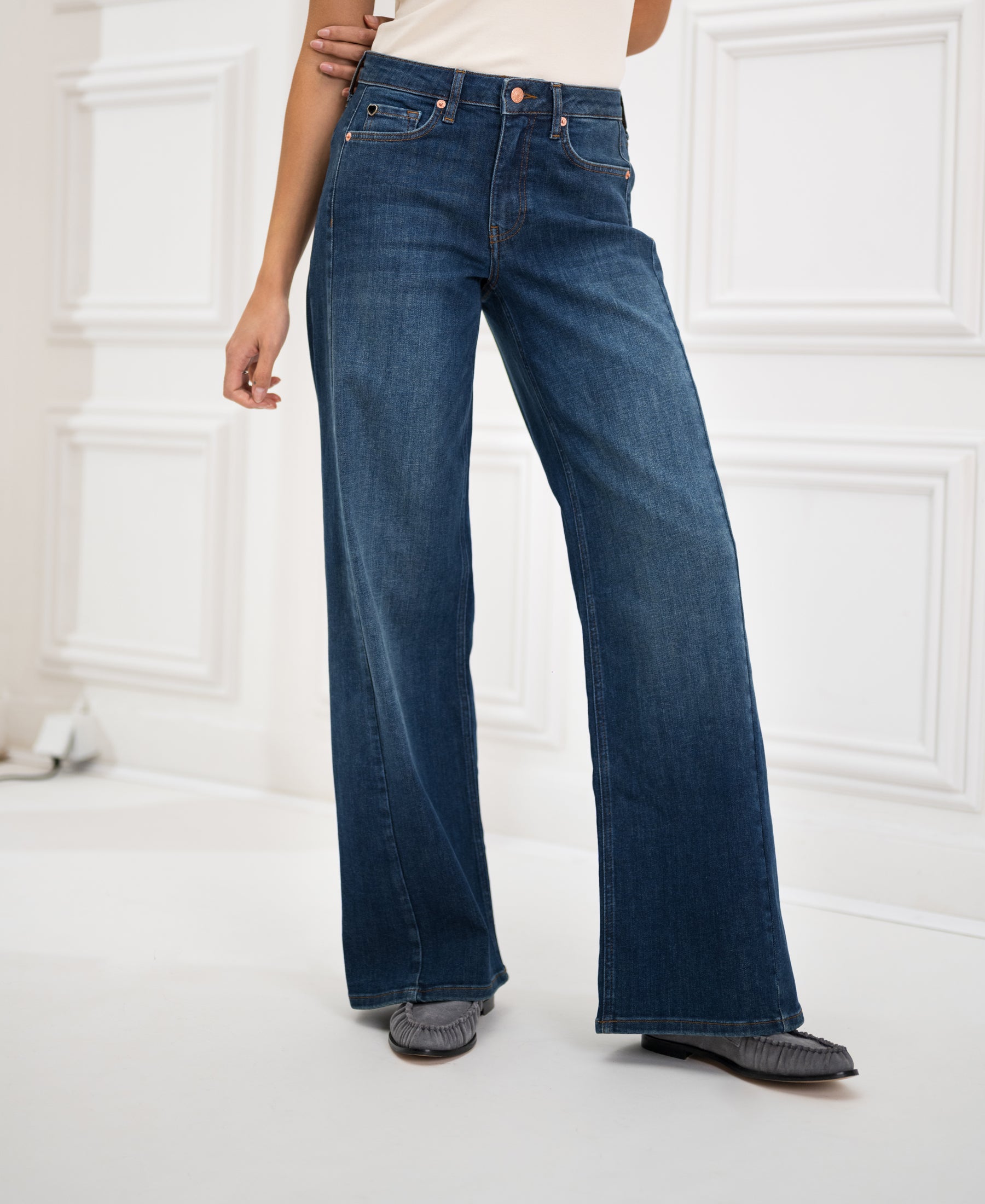 Wide leg jeans in blue, displayed in a white paneled room.