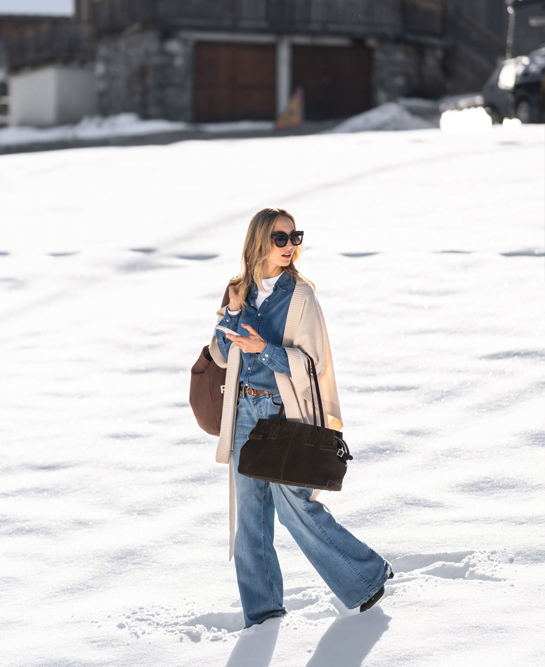 Wide leg jeans in light stone color, shown outdoors worn by a woman walking through snow past a building.