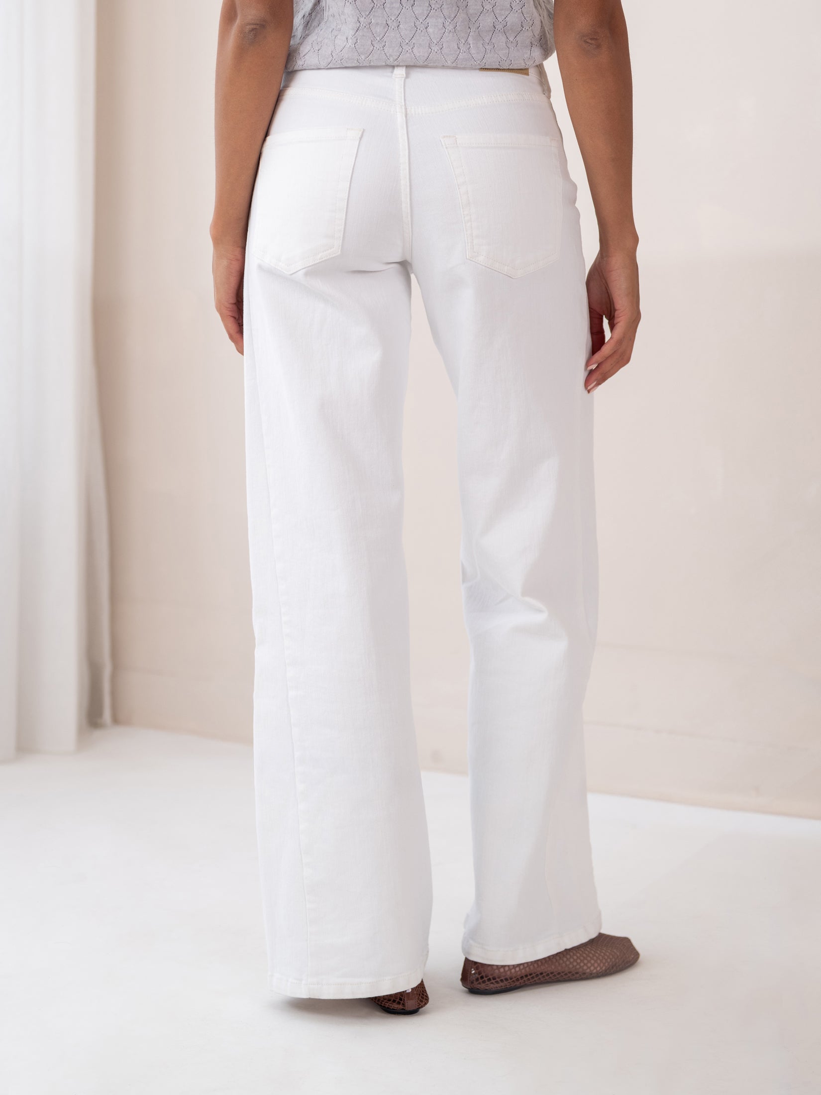 Back view of person indoors wearing wide leg white jeans.