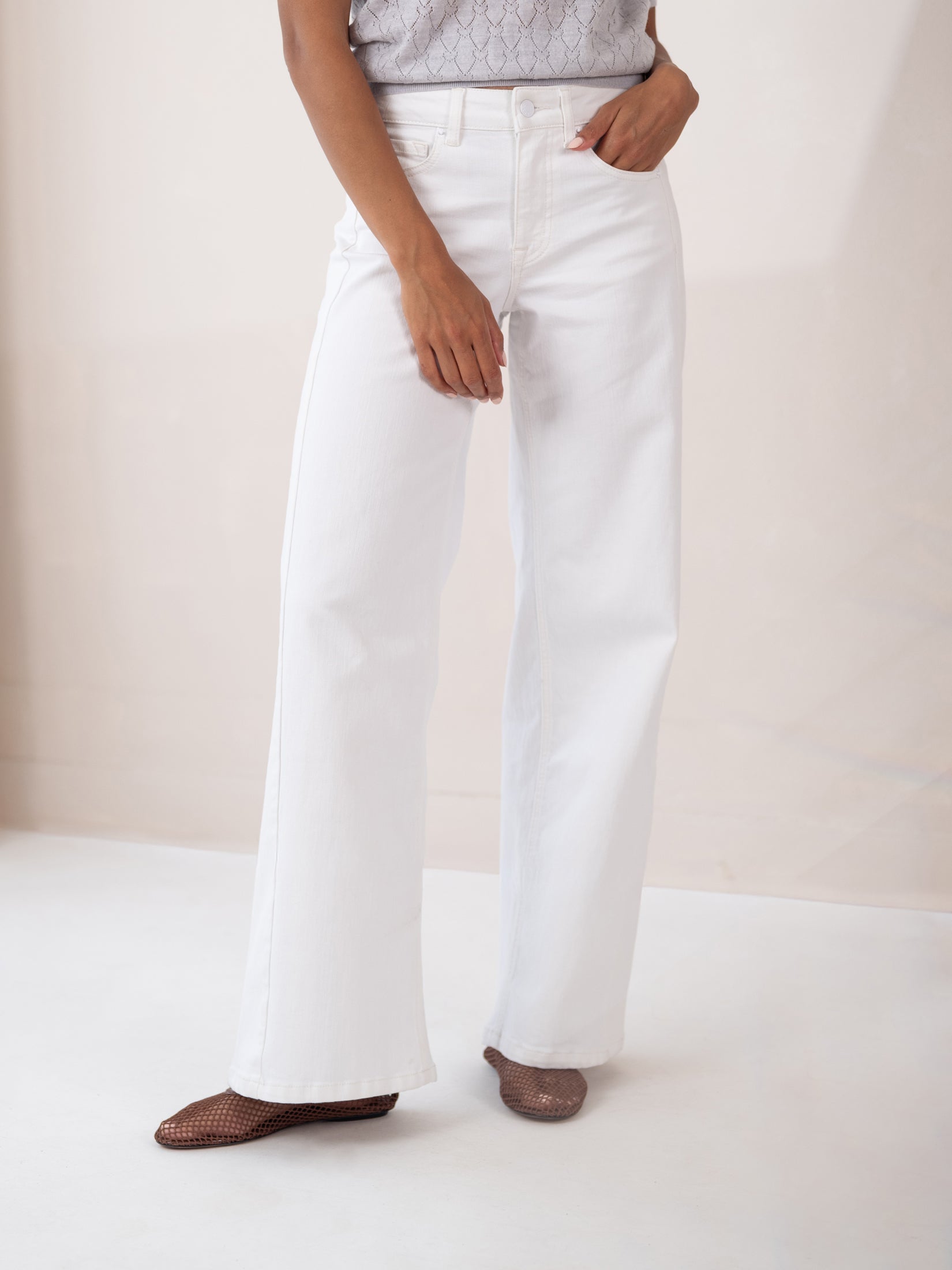 Model wearing white wide leg jeans, standing with one hand on hip.