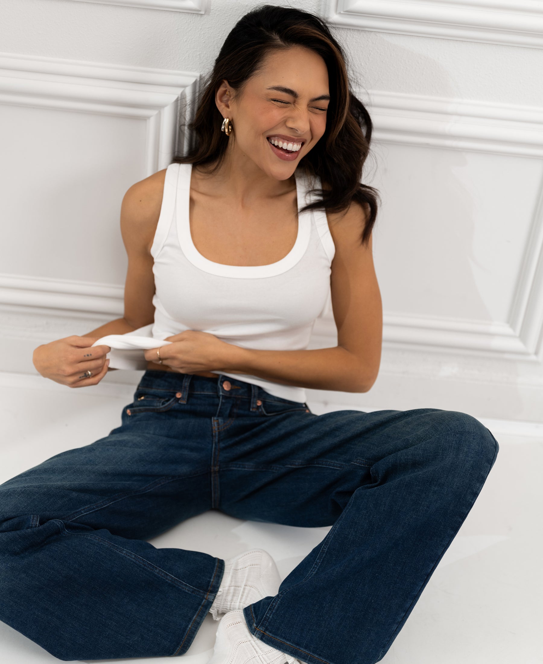 Woman sitting on the floor, laughing, wearing a PLEIN PUBLIQUE Luxe & Soft Top LA TOULON in white.