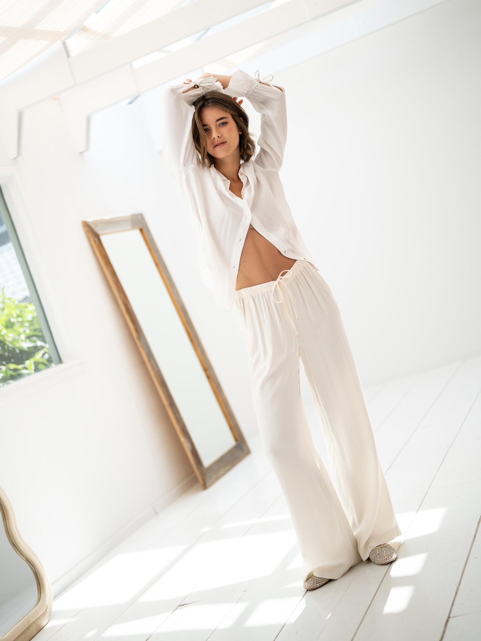 White LA TROYES blouse by PLEIN PUBLIQUE shown indoors with natural light, arms raised.