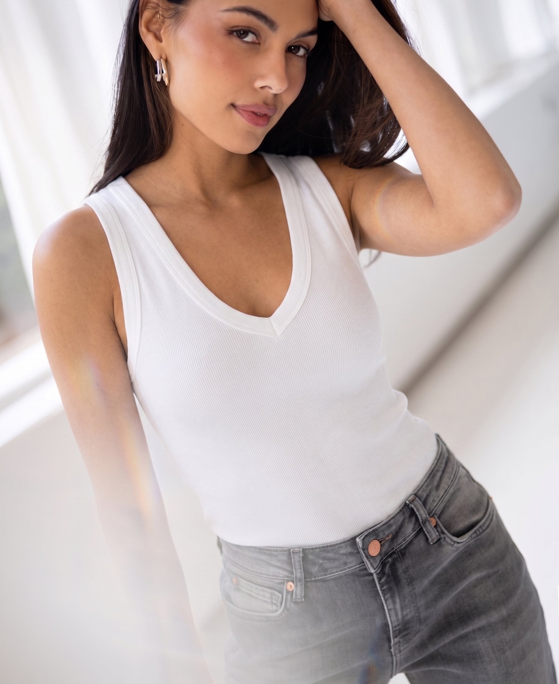 Woman wearing a luxe and soft white LA VALE top by Plein Publique poses indoors, touching her hair and looking at the camera.