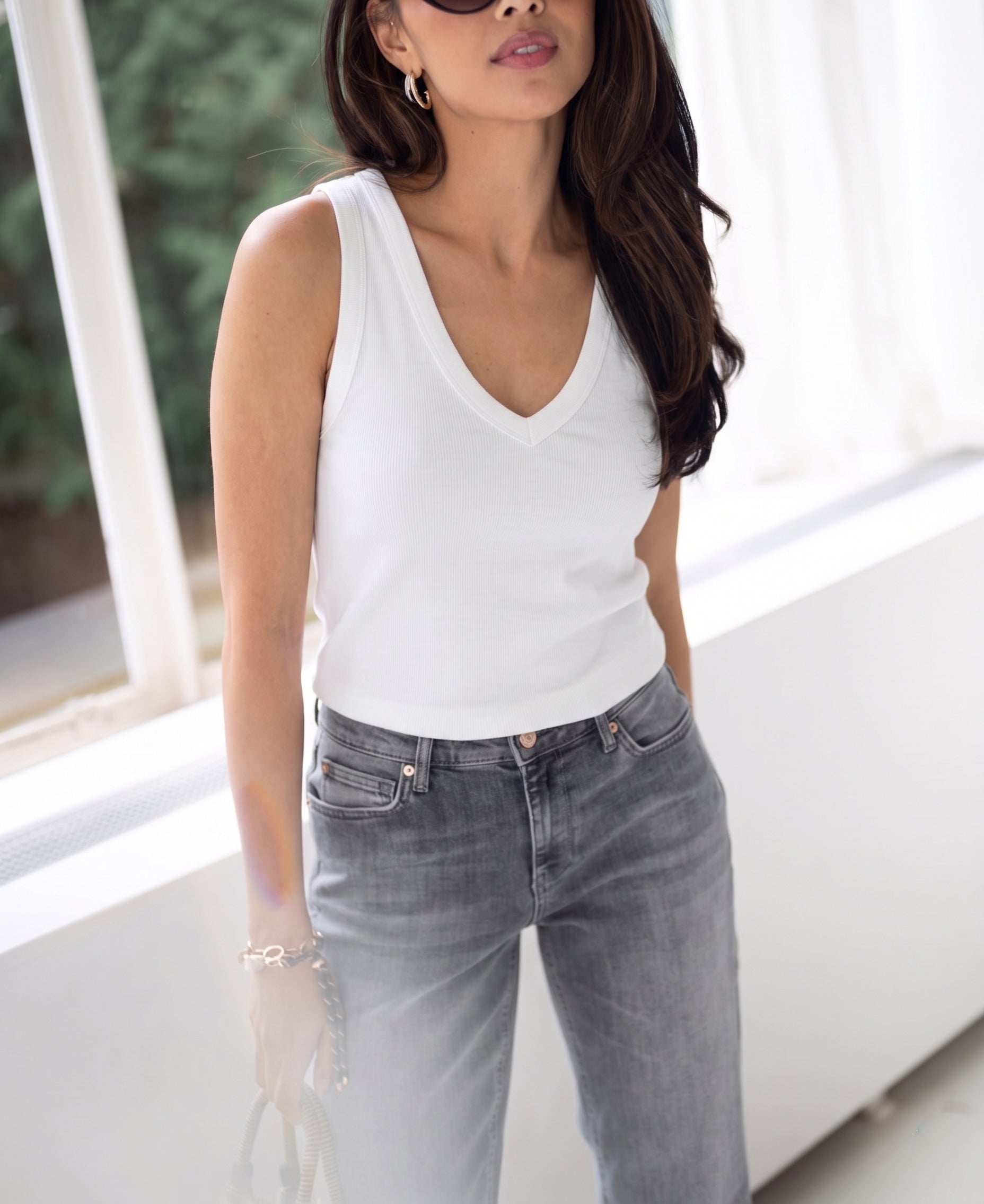 Woman wearing a luxe and soft white LA VALE top by PLEIN PUBLIQUE, standing by a window.