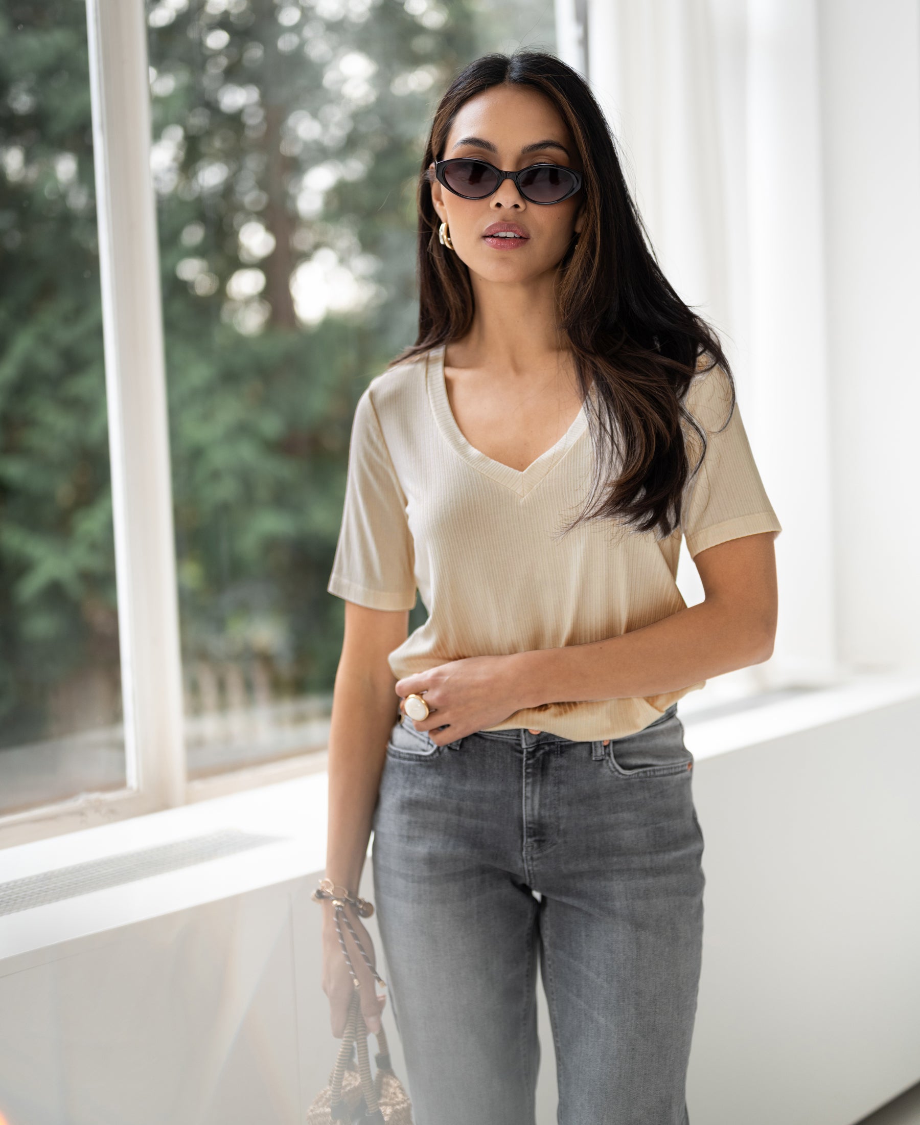 Woman wears a light sand bamboo T-shirt by a window with greenery.