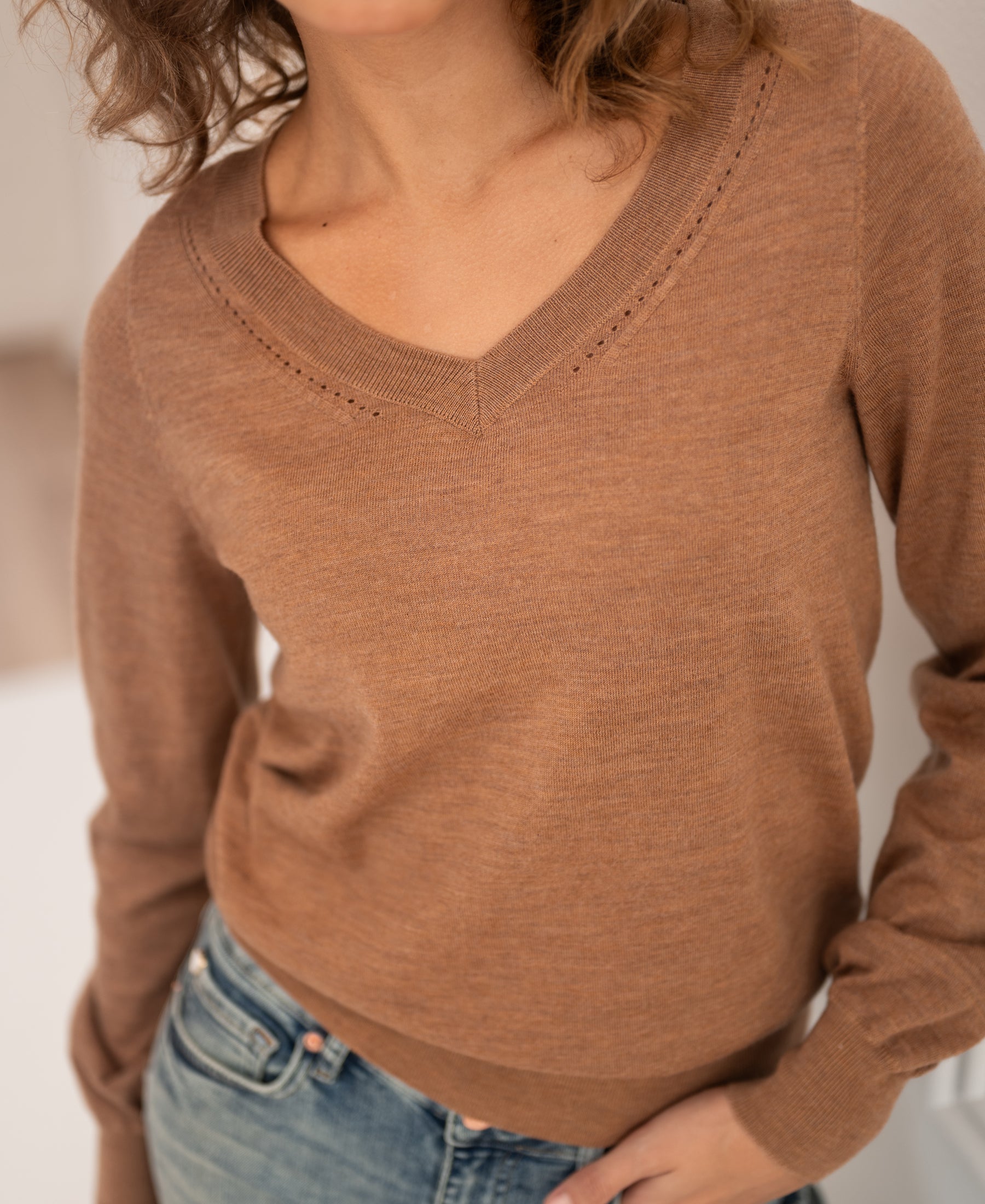 Merino wool V-neck sweater in Chai tea color by PLEIN PUBLIQUE, shown indoors with model’s face partly cropped.