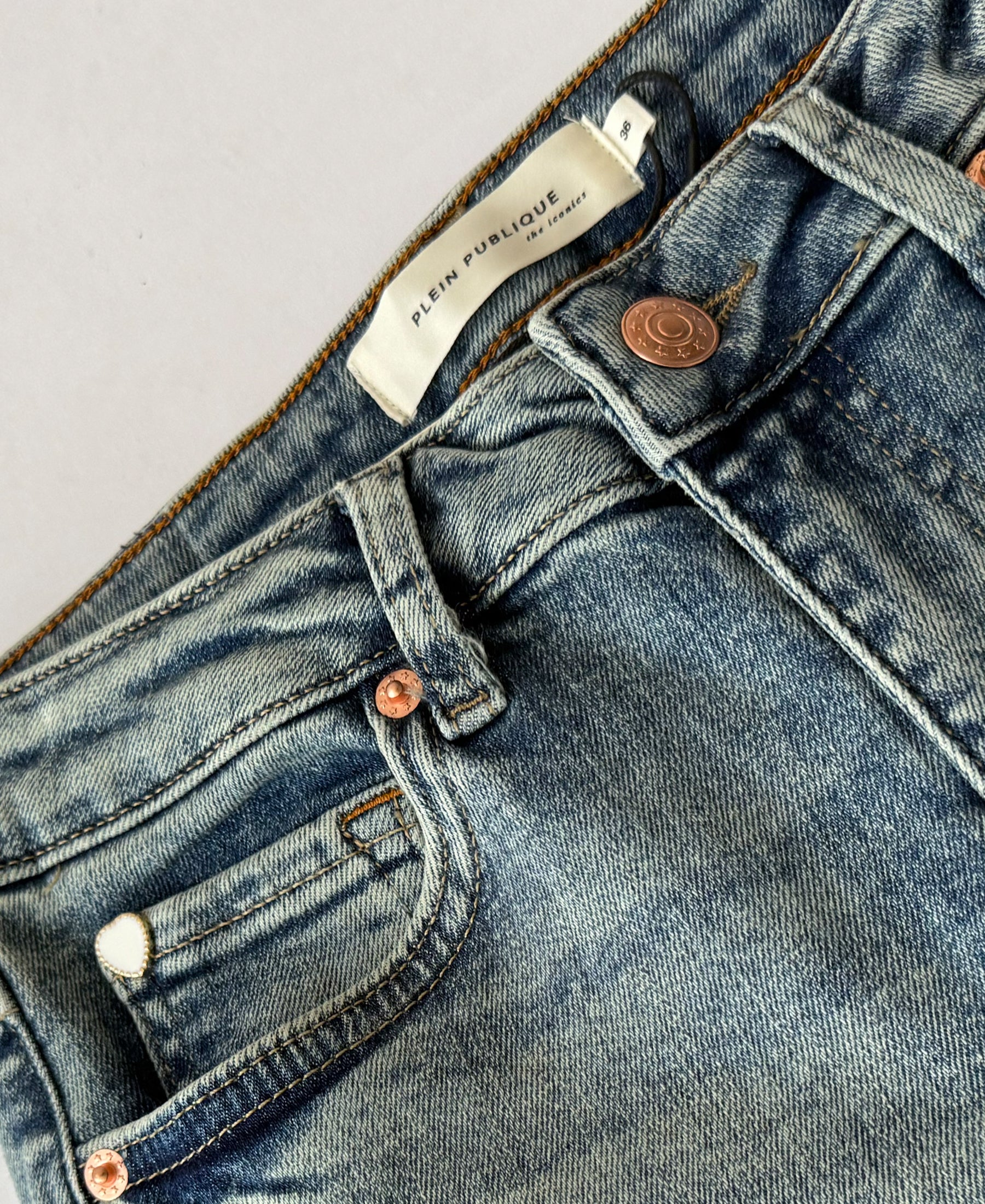 Close-up of wide leg blue denim jeans with copper buttons and a Plein Publique label.