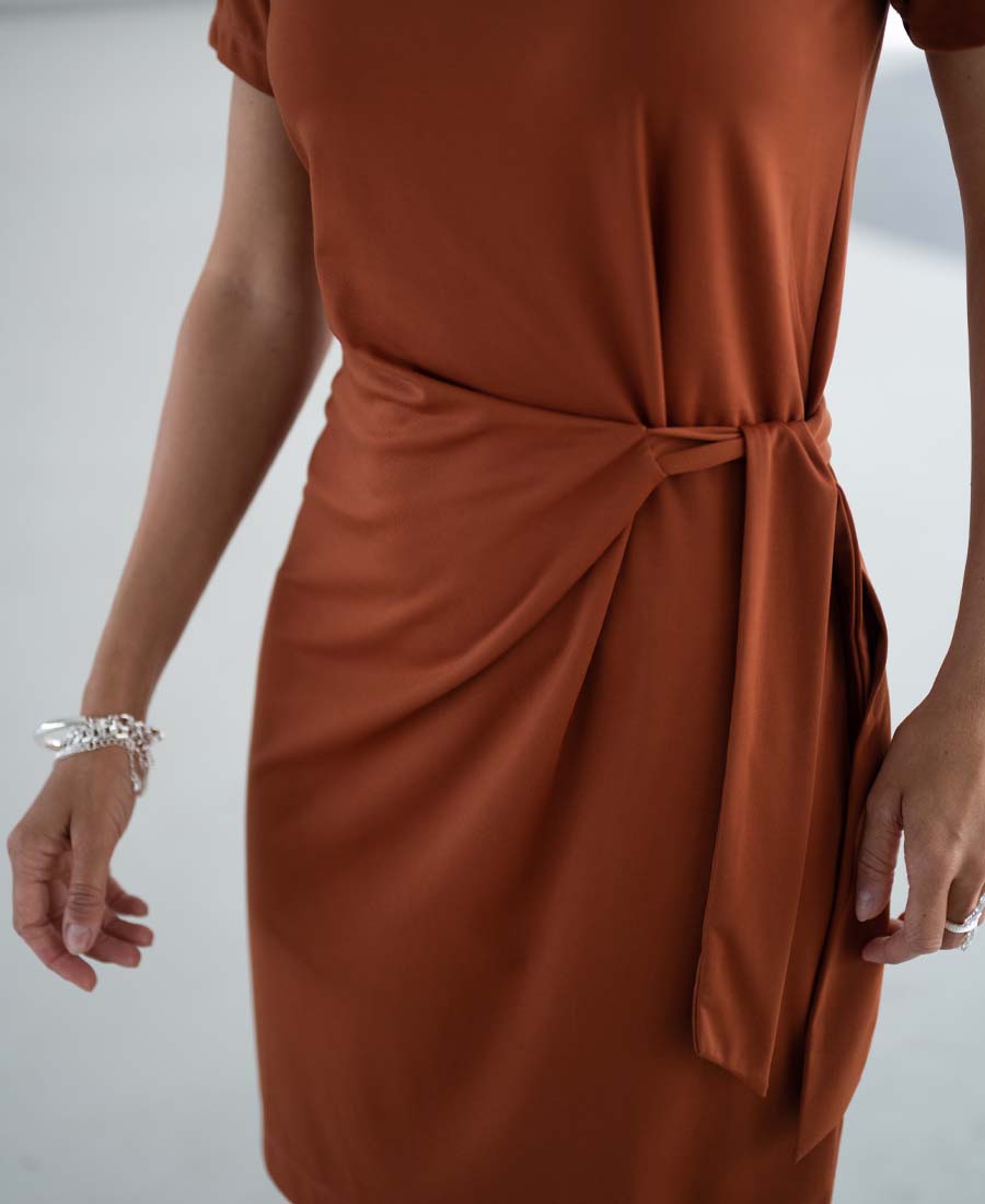 Woman wearing a terra-colored shirt dress with tied belt.