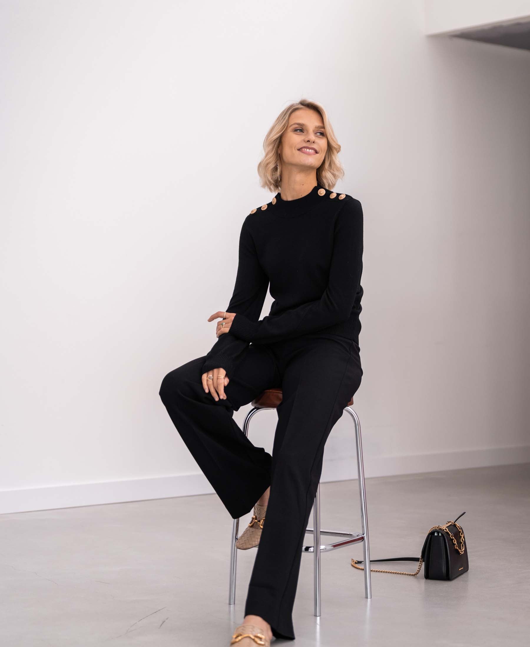 Black and gold merino wool sweater by PLEIN PUBLIQUE, LA CLIQUE style, shown on a seated model.