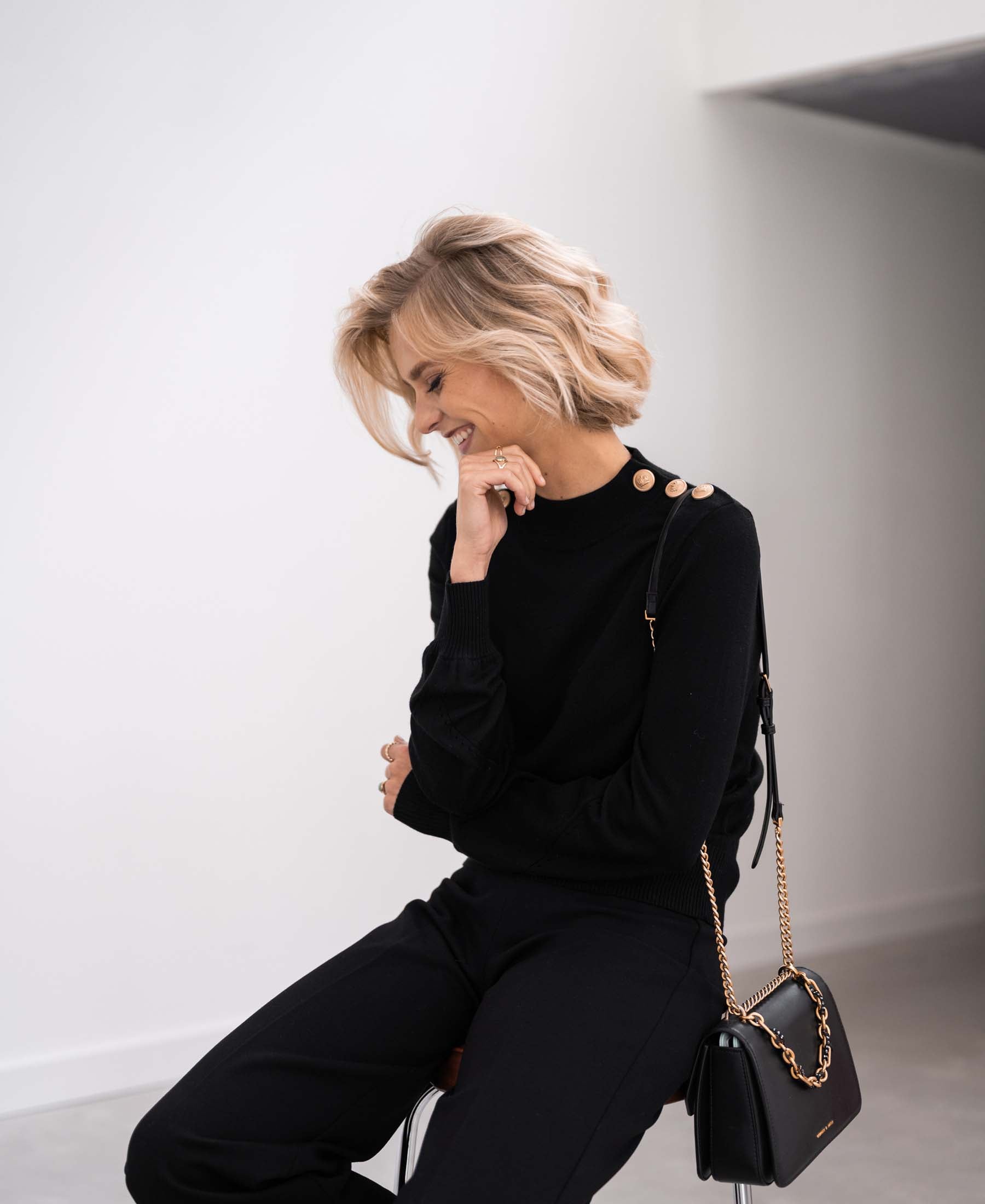 Black and gold merino wool sweater with long sleeves, shown on a model looking down and touching her chin.