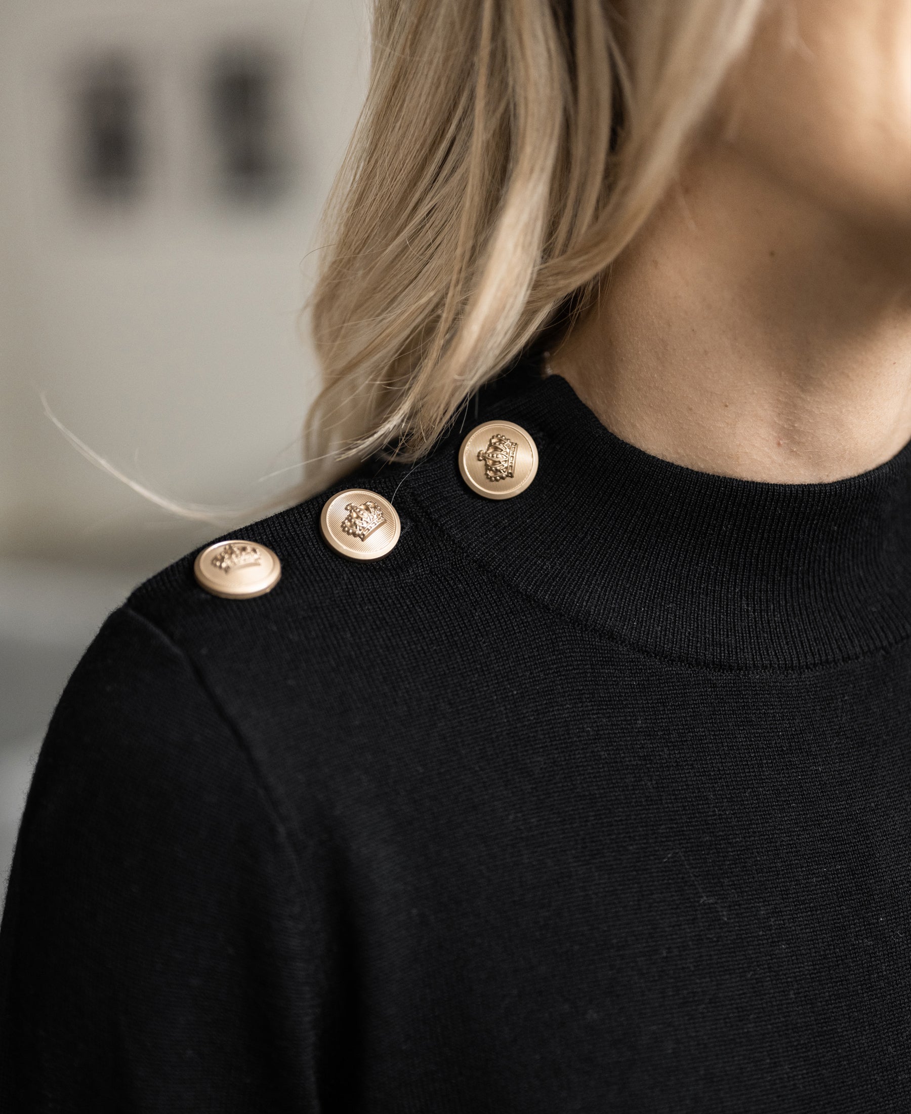 Close-up of the Merino wool sweater LA CLIQUE in black-gold by PLEIN PUBLIQUE, featuring gold shoulder buttons.