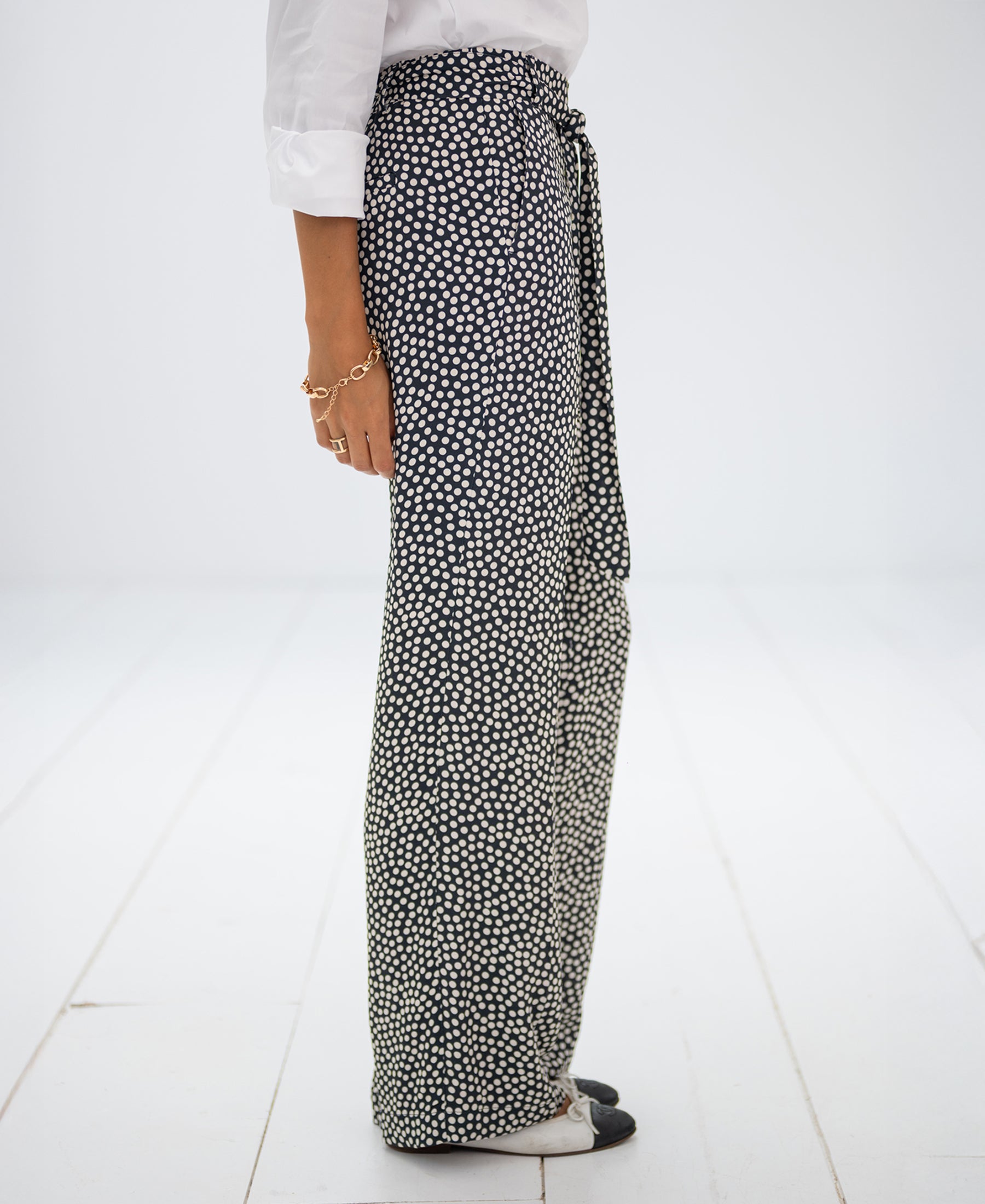 Side view of charcoal and ivory polka dot trousers on white floor.