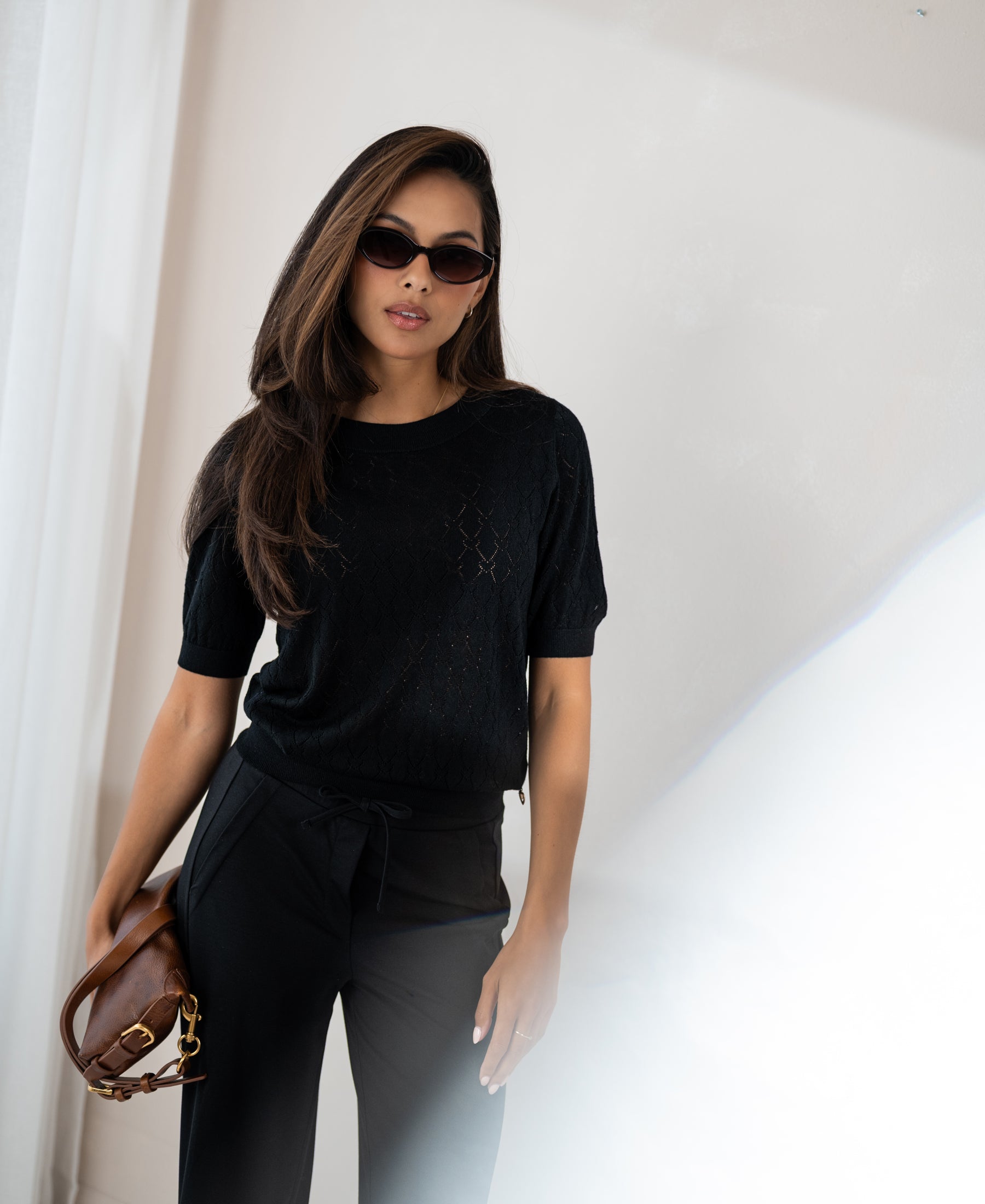 Black heart-patterned sweater by PLEIN PUBLIQUE, shown worn by a woman standing by a bright window.