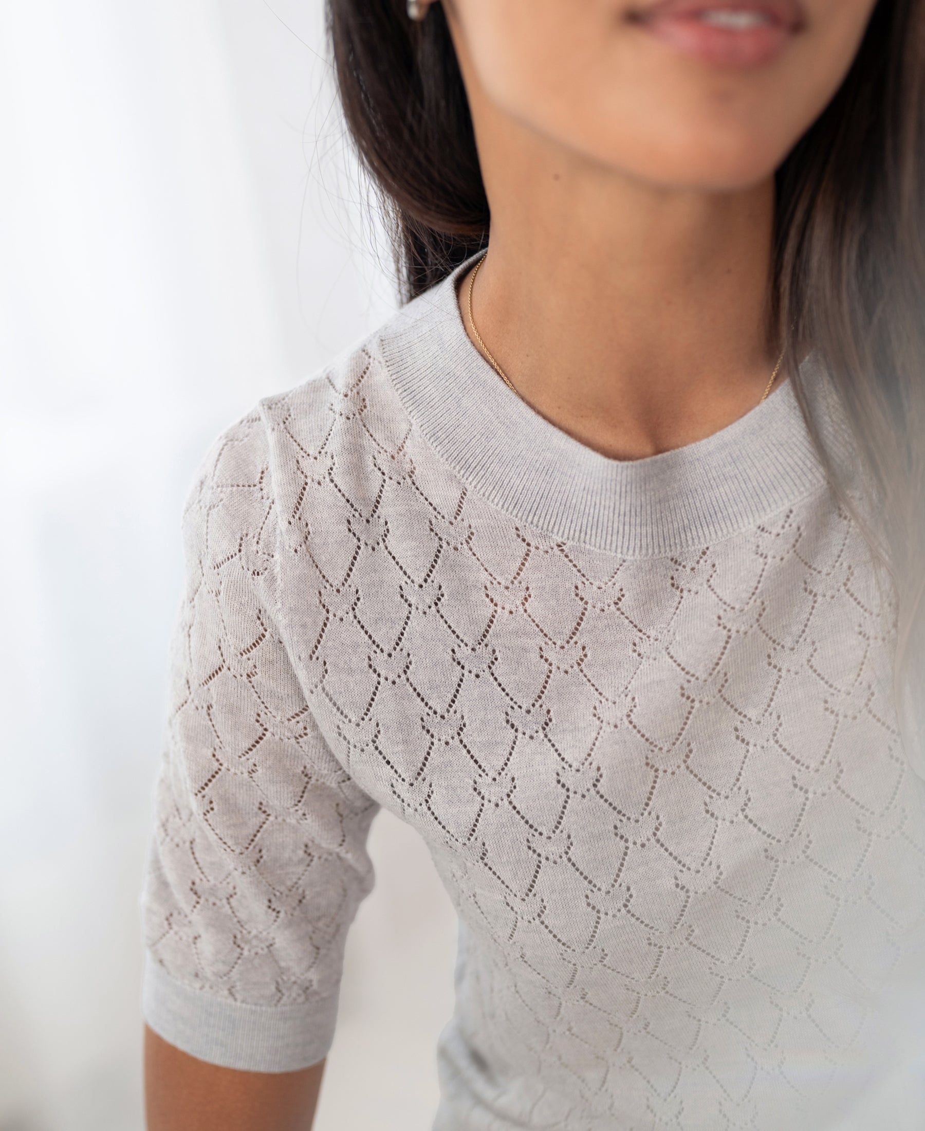 Light grey melange sweater with heart pattern by PLEIN PUBLIQUE, shown from the shoulders up.