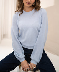 Light blue merino wool sweater from PLEIN PUBLIQUE, shown on a woman seated in soft light.