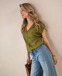 Sleeveless olive green blouse by PLEIN PUBLIQUE, shown on a woman in front of a light wall.