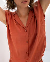 Sleeveless blouse in terra color with supple fabric, shown with arms raised to display the fabrics drape.