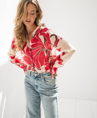Woman wearing LA Binocle blouse with ruby red print, standing in sunlight with hands on hips and looking down.
