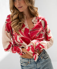 Ruby Red print blouse with LA BINOCLE design, shown in soft natural light, modeled with hand on waist.