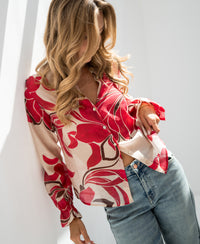 Ruby Red print blouse with a relaxed fit, shown on a woman standing beside a white wall.