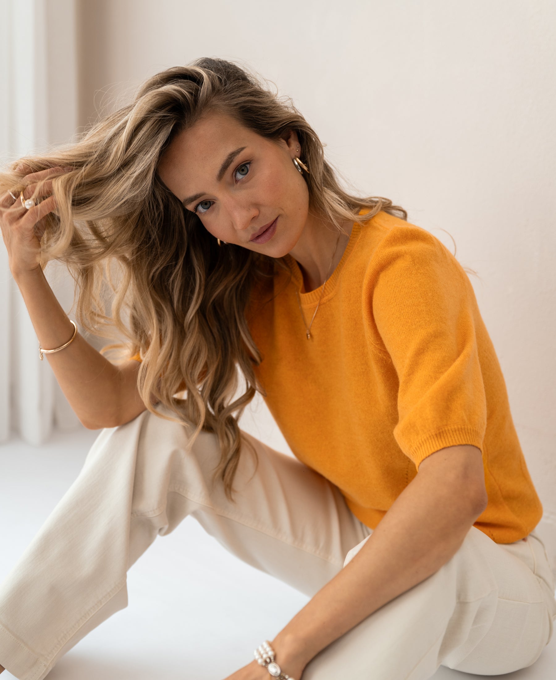 Woman wearing PLEIN PUBLIQUE LA BLANCHE orange sweater sits on the floor.