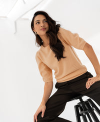 Woman wearing a soft salmon-colored sweater sits in a bright, minimal room.