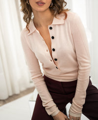 Woman wearing a butter blush Merino wool polo shirt by Plein Publique, seated indoors.