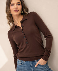 Woman wearing a Plein Publique merino wool polo shirt in cocoa stands against a light wall, facing the camera.
