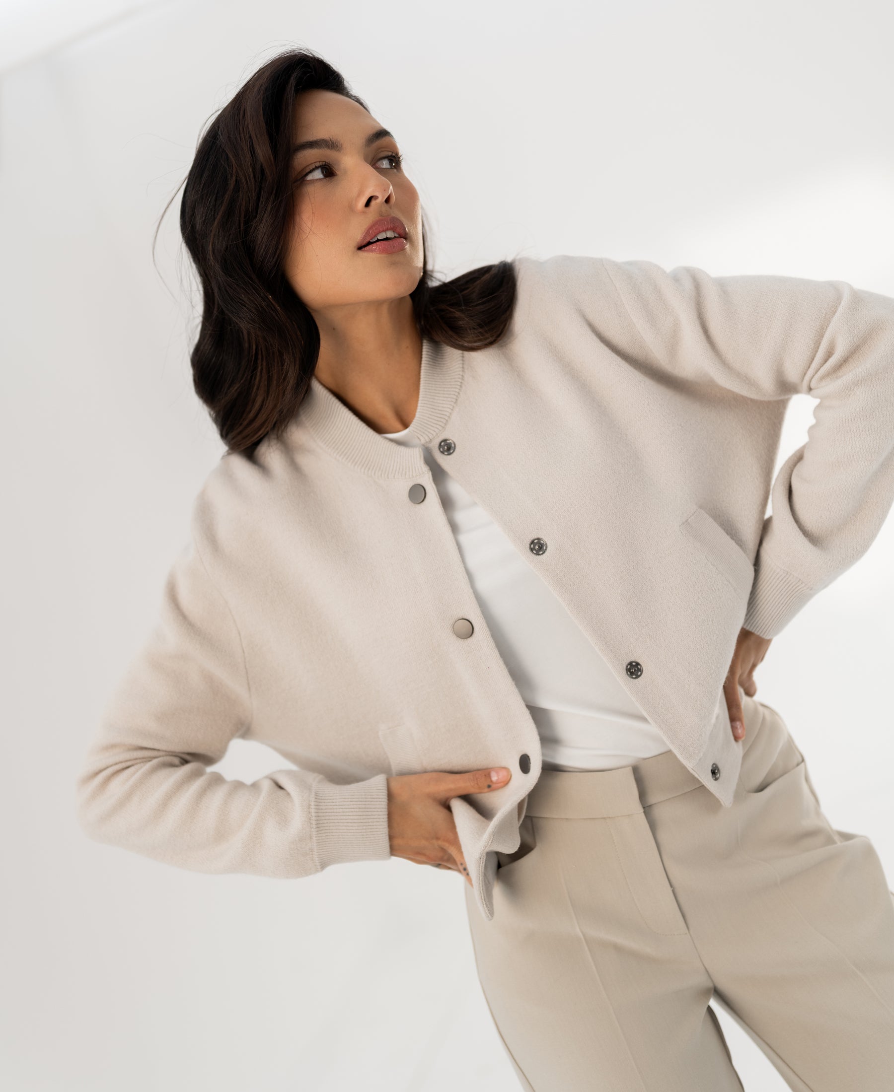 Beige bomber jacket in a side view, shown with one hand on waist.
