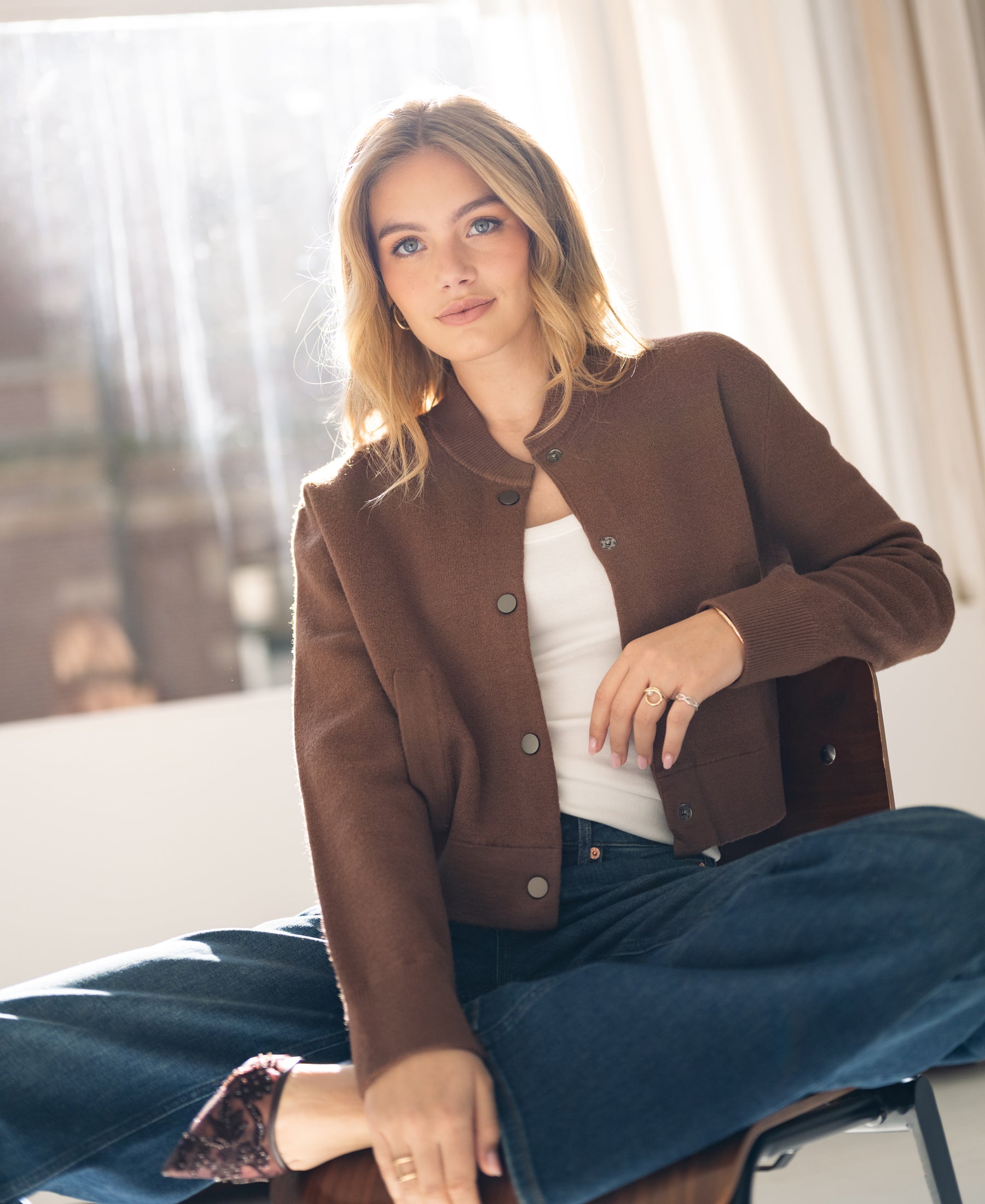 Camel bomber jacket in sunlight, shown worn by a woman sitting cross-legged.