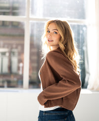 Camel-colored women's bomber jacket, shown from the back and side near a window.