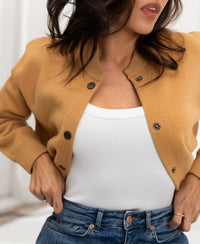 Light camel bomber jacket in a relaxed fit, shown worn by a woman with hands on waist.