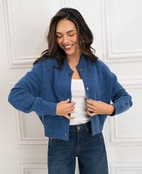 A woman buttons a blue denim bomber jacket.