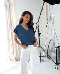 Woman wearing a ribbed LA BONNE denim blue T-shirt by PLEIN PUBLIQUE poses in a bright studio.