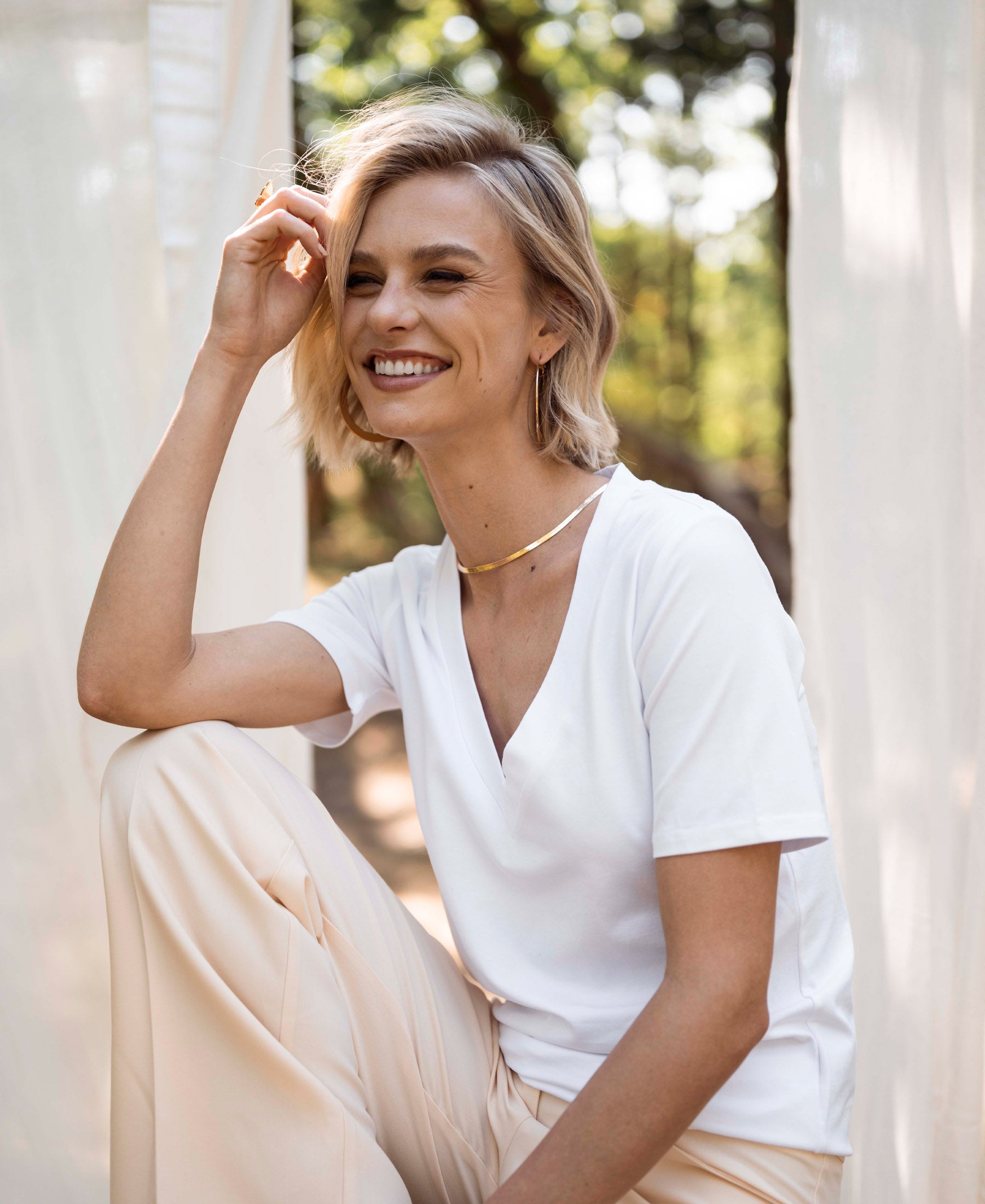 White V-neck T-shirt LA VIDA by PLEIN PUBLIQUE, shown outdoors among sheer curtains.