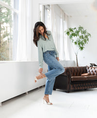 Cropped jeans in light stone color are shown being worn in a bright living room.