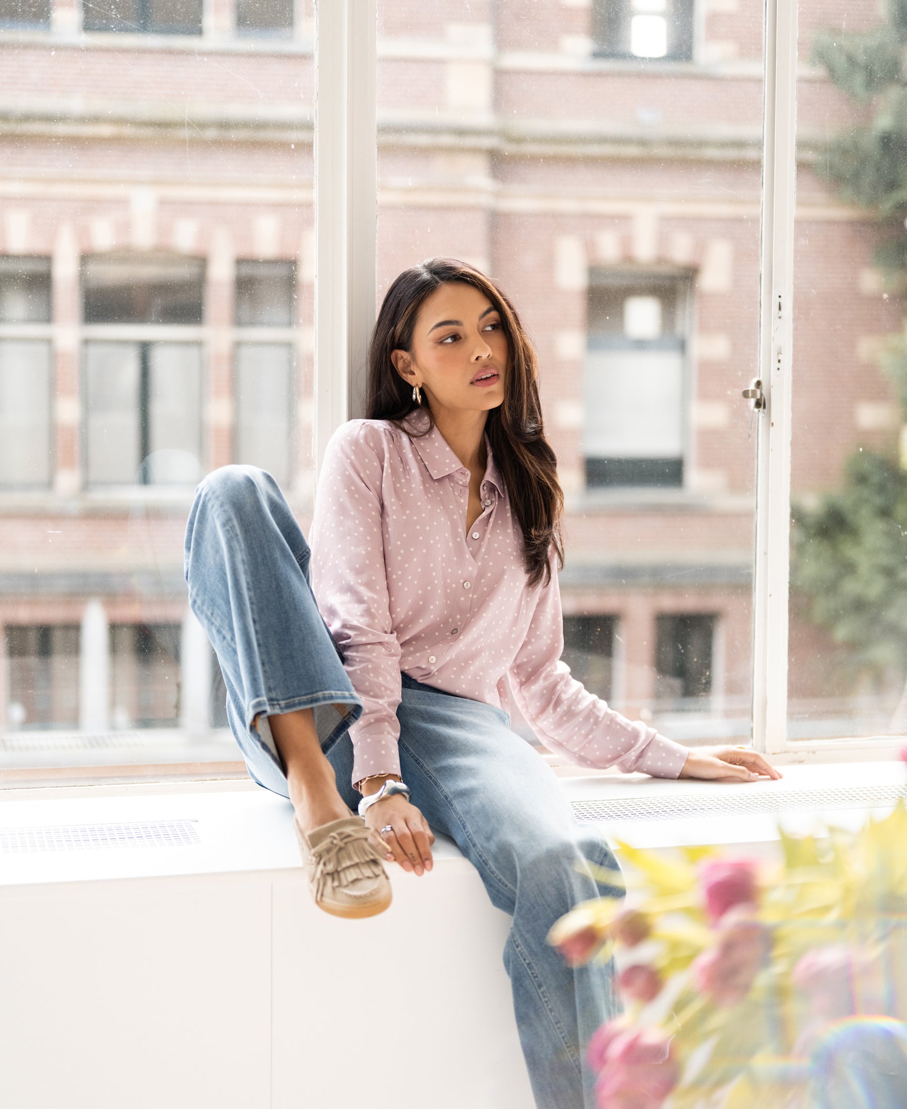 Dusty pink and ivory polka dot blouse, shown worn by a woman seated indoors. Brick building visible, blurred in background.