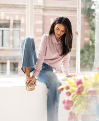 Dusty pink polka dot blouse in ivory from Plein Publique, shown worn by a woman sitting on a windowsill.