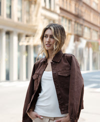 Woman wearing a PLEIN PUBLIQUE stretch denim jacket LA CALLAS in cacao stands on a city street with blurred background.