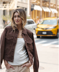 Woman wearing a PLEIN PUBLIQUE stretch denim jacket in cacao brown, seen from the front.