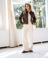 Stretch denim jacket in cocoa brown from PLEIN PUBLIQUE, shown indoors by a window.