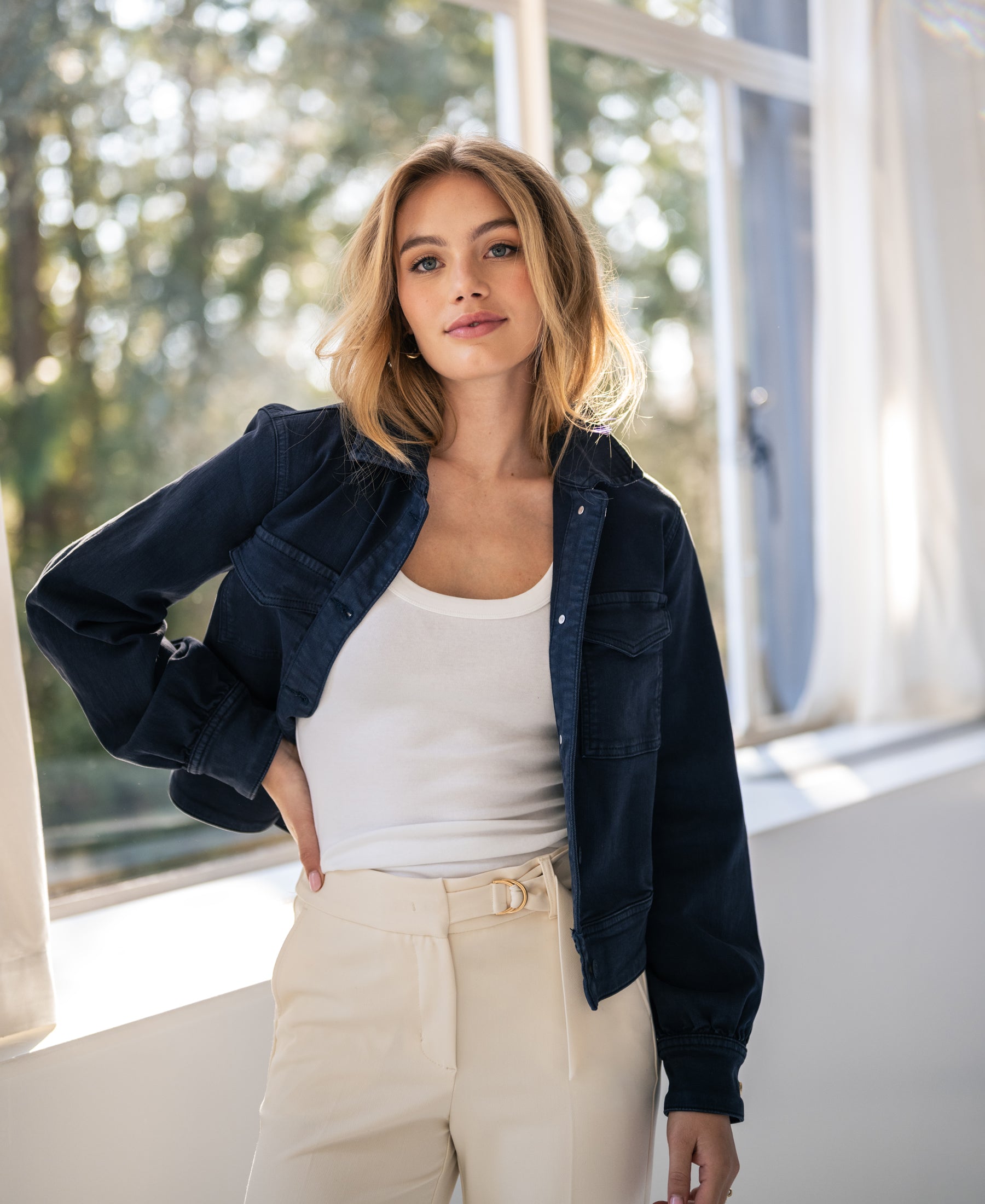 Woman wearing the PLEIN PUBLIQUE dark blue stretch denim jacket LA CALLAS by a window.