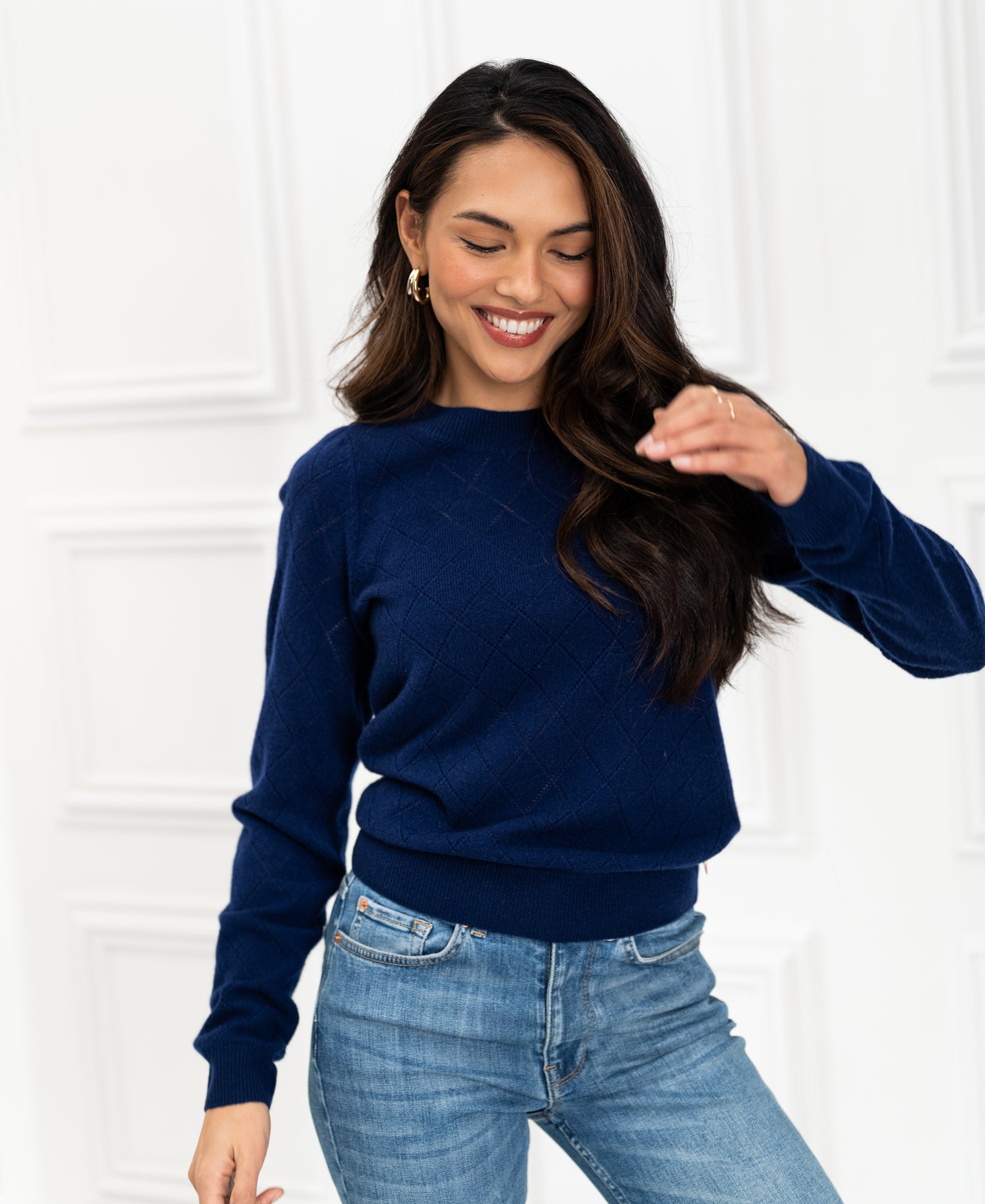 Front view of woman wearing a navy argyle merino wool sweater against a white paneled background.