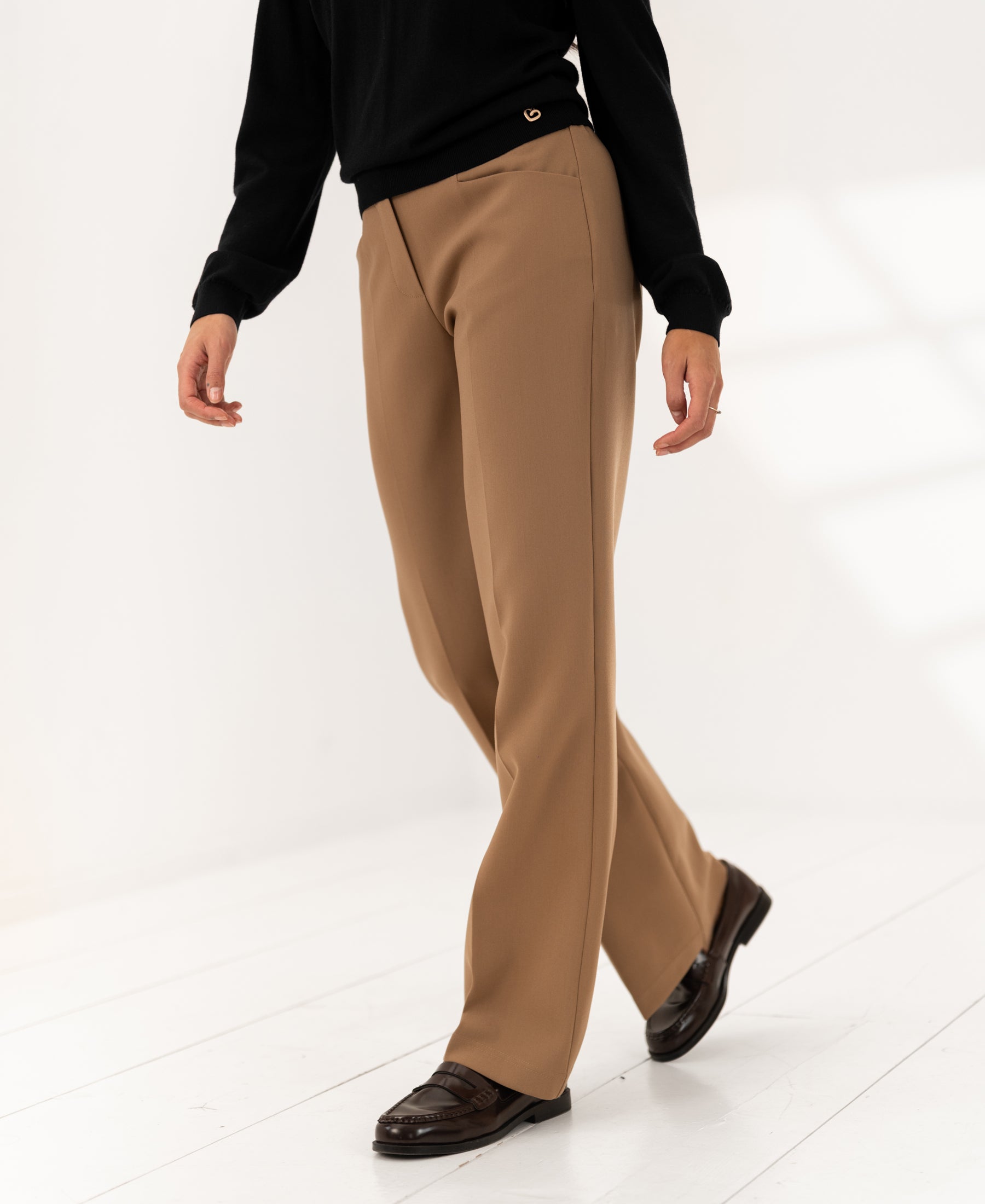 Person wearing wide-leg LE CENTRE camel pants by PLEIN PUBLIQUE standing on a sunlit white floor.