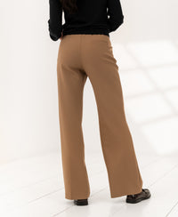 Person wears PLEIN PUBLIQUE LE CENTRE wide-leg trousers in camel, on white floor, facing away.