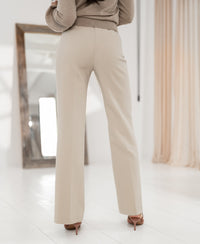 Wide-leg trousers in light beige, shown standing in a bright room with a large mirror and curtains.