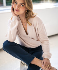 Woman wearing a PLEIN PUBLIQUE wrap sweater LES CINQ in soft blush, facing the camera and smiling.