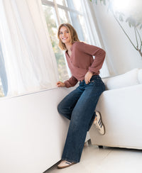 Woman wearing the LES CINQ Wrap Sweater in desert rose by PLEIN PUBLIQUE, smiling by a window.