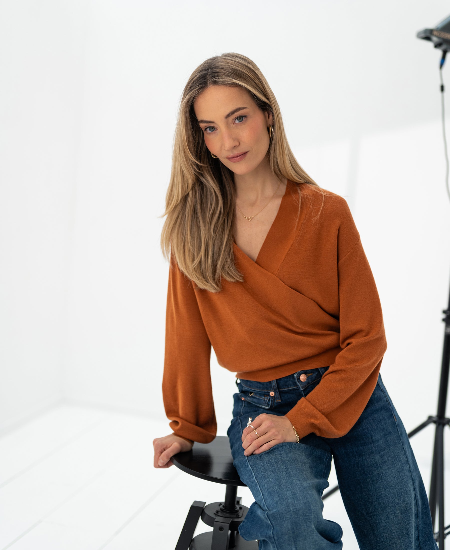 Woman with long blonde hair wears the PLEIN PUBLIQUE wrap sweater LES CINQ Terra in a bright, white studio.